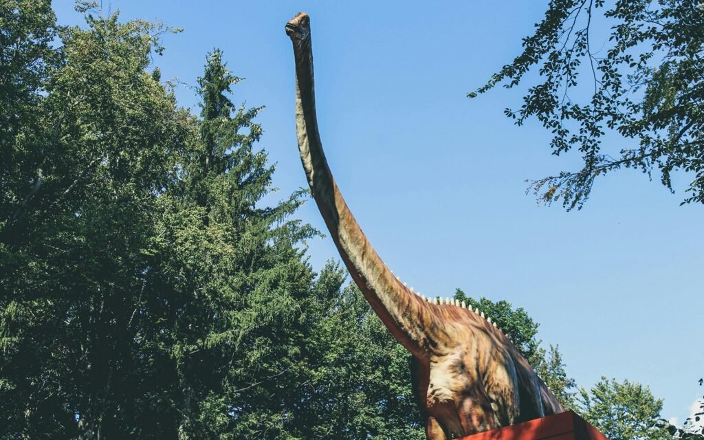A large dinosaur statue in an outdoor park surrounded by greenery and blue sky.